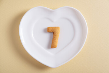 Biscuits forming number 7 on the white plate and yellow light background