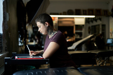 Caucasian tattoo artist sitting at the studio and making new project