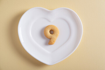 Biscuits forming number 9 on the white plate and yellow light background