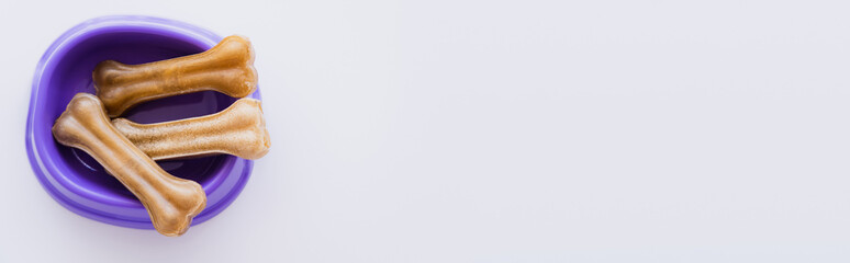 top view of bone shaped pet treats in purple bowl isolated on white, banner.