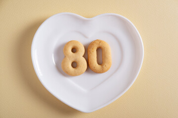 Biscuits forming number 80 on the white plate and yellow light background