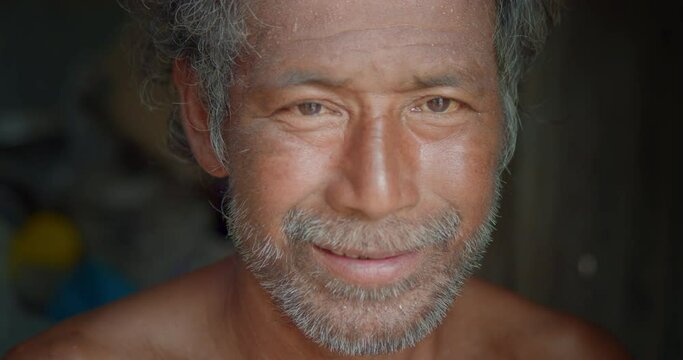 Happy smiling male Asian farmer and mercenary man with beard who is an old poor indigenous man, live in a small shabby old house. The cover of the house is galvanized sheet.