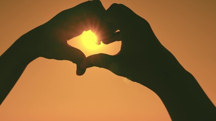 silhouette of the heart in the rays of the sun. make heart symbol with hands. valentine. love sign. freedom of travel. happiness of a woman's dream. heart against the sky. declaration love to person.