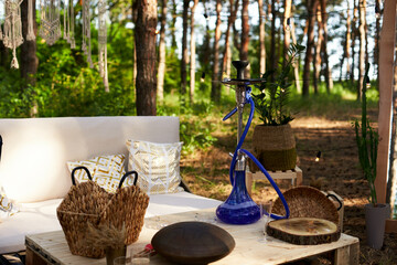 Lounge zone with hookah, diy sofa and table of cargo pallets in boho style on outdoor wedding ceremony venue in pine forest. Bohemian decor.