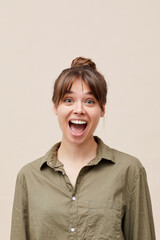 Portrait of expressive young woman with bangs and hair bun screaming loudly in excitement