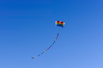 Multicolored rainbow kite with tail flying in blue sky