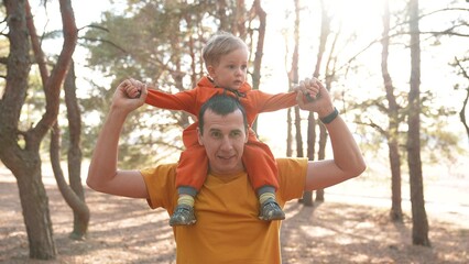 Obraz premium father and son in the park. happy family piggyback a kid dream concept. father holds baby son keeps on the neck in a forest park close-up. baby and parent man happy family fun walking in nature