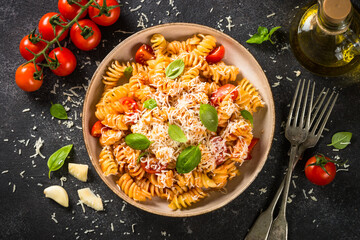 Italian pasta alla arrabiata with basil and parmesan cheese on dark table. Fusilli pasta with tomato sauce arrabbiata. Top view.
