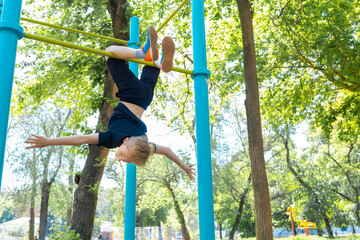 the boy caught his feet on the horizontal bar and hangs upside down he is in the park
