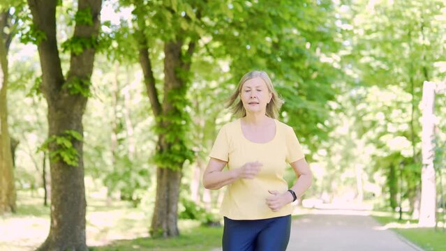 Senior active gray-haired woman morning jogging in the urban city summer park outdoor. Mature old fitness female running exercise. Healthy Lifestyle. Elderly sport runner woman training Workout cardio