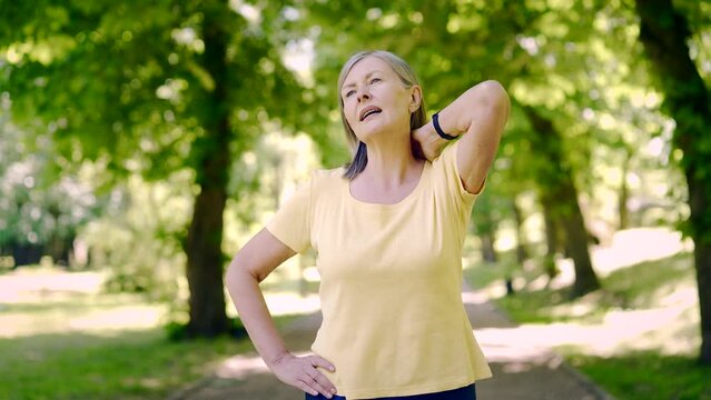 Senior retired woman neck or back pain during workout jogging outdoors in the park. Muscle ache during sports exercises. Mature sports fitness female suffering from pain. Massages hurt shoulder