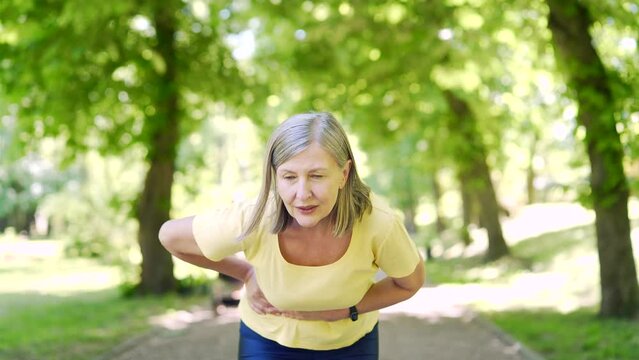 Sport Senior woman having stomach ache in the park outdoors while jogging work out. Mature female suffering having abdominal pain sudden. old runner having cramps after running training