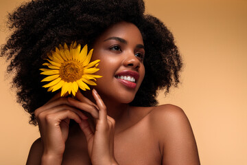 Optimistic young African American woman putting sunflower in hair and smiling