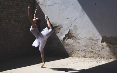 Young ballerina in white tutu dancing and jumping in abandoned building on a sunny summer day