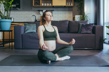 Obraz premium A pregnant woman meditates and practices yoga in a lotus position at home