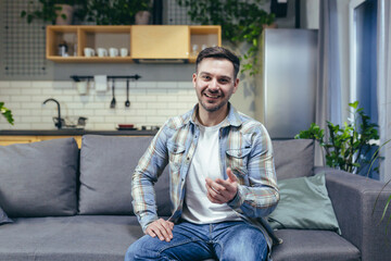 Fototapeta premium A man at home sitting on a sofa looking at the camera, a porter talking on a video call