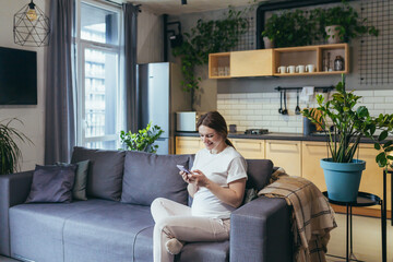 Obraz premium Pregnant woman at home uses the phone while sitting on the couch