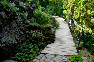 wooden bridge with forged metal railing. The bridge goes over a stone rock over an abyss in a gorge. the planks are thoughtfully dodging the stone that the carpenter had them toothed around. board