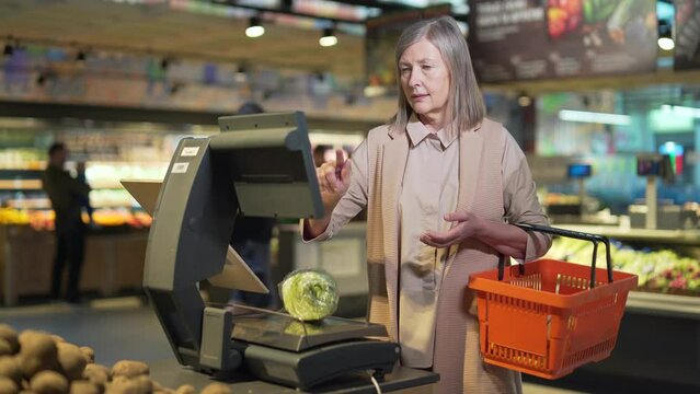 Senior mature retired woman shopper weighs groceries, vegetables in supermarket, grocery store. old female retiree the customer or buyer makes daily purchases on scales on food market