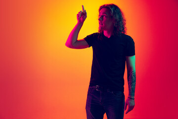 Young emotional man with long curly hair posing isolated on yellow red background in neon. Human emotions, facial expression concept. Trendy colors