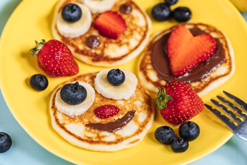 American pancakes decorated like smile and happy faces with strawberries, chocolate, blueberries and banana. Food for kids, playful and creative.
