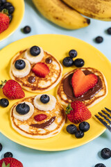 American pancakes decorated like smile and happy faces with strawberries, chocolate, blueberries and banana. Food for kids, playful and creative.