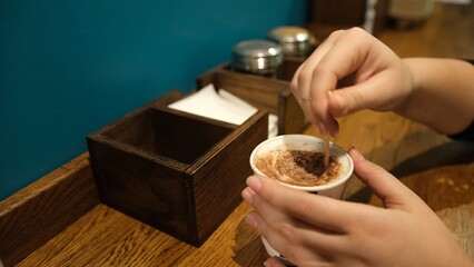 A woman holding coffee with cream and wooden stick and stirring hot coffee on wooden table