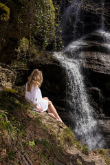 Fototapeta na wymiar blonde woman in white dress sitting looking at a waterfall