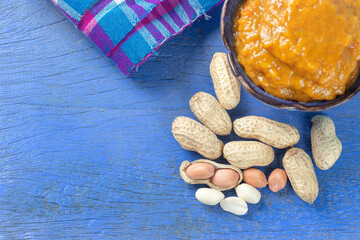Bowl of peanut butter and spoon of peanut butter and peanuts on blue wooden background