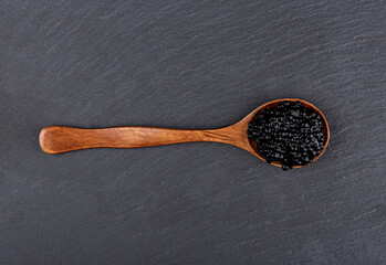 Top view of a wooden spoon with black caviar over a stone serving board.