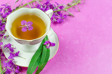 Drink (infusion, decoction) from ivan-tea in a white cup on a saucer on a bright pink background. A place for a text, a recipe. Grass and flowers of the plant kipreya, ivan-grass, epilobium.