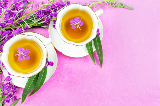 A drink (infusion, decoction) of ivan-tea in a white cup on a saucer on a pink background. Grass and flowers of the plant kipreya, epilobium, ivan-grass. Space for the text.