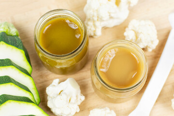 Two glass jars with children's pureed cauliflower and zucchini puree on a wooden background. The first lure of the baby. Baby food.
