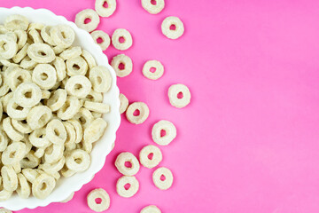 A bowl with oatmeal (corn) rings on a bright pink background. Space for the text. Dry healthy breakfast, add milk.