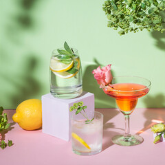 Refreshing colorful summer drinks on pink and light green background with shadow and flowers. Varios cocktails with various fruits: orange, grapefruit, lemon. Pop-art aesthetic, square crop