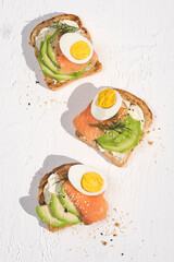 Summer healthy fastfood lunch, breakfast with light soft cheese sandwich, red fish, avocado and egg, white background. Aesthetic still life, healthy food concept