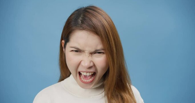 Portrait of a frustrated angry pensive Asia lady open mouth scream out loud isolated on the blue background. Crazy female bad mood argument shouting at boyfriend, Negative emotions and feeling.