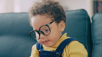 Funny African American toddler in huge eyeglasses sitting on sofa, cute baby