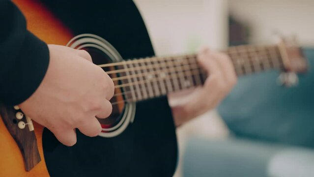 Caucasian male playing acoustic guitar at home, hands close-up, musical hobby