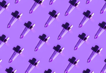 Pipette with gold metallic cap and drops of water, serum, oil, beauty product on violet background. Natural medicine, cosmetic research, bio science. Concept of skincare, analysis. Flat lay, pattern