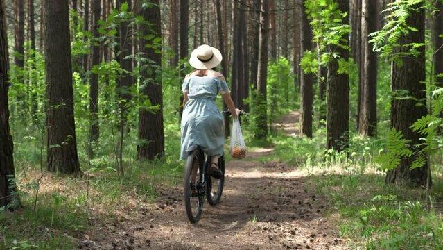 Woman rides a bicycle with a wicker string bag of fresh fruit. Life without plastic waste. Low waste lifestyle. Sustainable ecological lifestyle