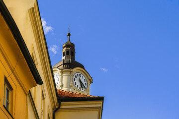 Old double clock on the tower of a medieval building behind yellow vintage walls against a blue sky on a sunny day, the passage of time. Copy space on the right
