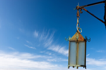 Close-up of a medieval street lamp made in in wrought iron and glass, against a clear blue sky and clouds. Tellaro village, Lerici municipality, La Spezia, Liguria, Italy, Europe.
