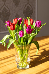 Glass vase on the table with tulips, light from the window and shadows. Place for text, romantic. The concept of birthday, holiday, romance, good morning, mother's day, March 8, valentine's day,