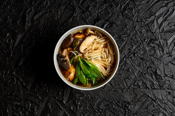 Mushroom soup udon noodles with fresh green onions in a fine white bowl against a black design...