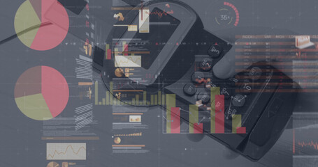 Image of graphs and financial data over hand of caucasian man holding payment terminal