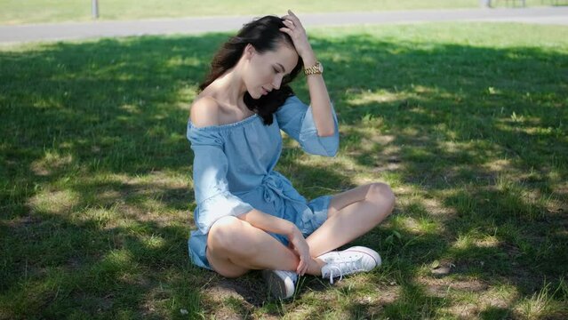 Portrait of attractive brunette woman in blue dress sitting in a park