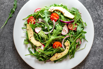 Vegan food. Healthy fresh vegetable salad - tomatoes, arugula, avocado, radish on a stone background. Diet menu.