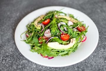 Vegan food. Healthy fresh vegetable salad - tomatoes, arugula, avocado, radish on a stone background. Diet menu.