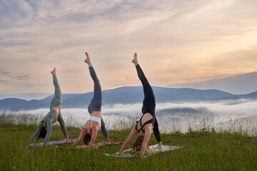 Group of three young women in sport clothes having yoga practice with amazing view on mountains. Concept of people, training and healthy lifestyles. 
